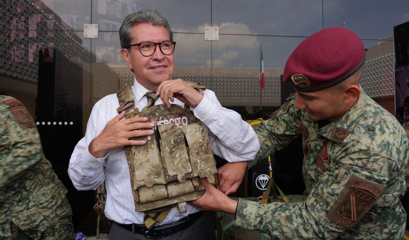Ricardo Monreal ajusta un chaleco táctico con ayuda de un militar durante una exhibición.
